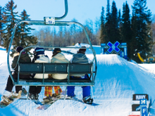 Snowboarders take a high-speed quad chairlift to the top of a run at Aspen