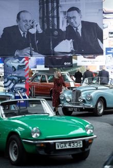 A visitor admires one of the cars surrounded by period advertising material reproduced onto giant banners hanging above the cars st Great British Car Journey in Ambergate Derbyshire, .