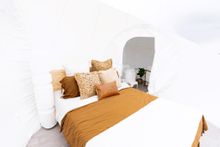 Interior of natural linens and queen bed in the Captain Moonline Mirumiru Bubbletent. The interior bathroom and composting toilet is part of Mirumiru Bubbletents eco-friendly stay.