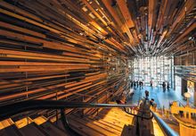 Image: Interior of the Nishi Building's Grand Staircase warmly lit and surrounded with disjointed, layered wooden panelling at Canberra's NewActon precinct. 