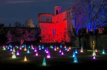 Spectacle of Light Christmas Light Trail at Sudeley Castle in The Cotswolds. Photo shows the Richard III Banqueting Ruins illuminated in red and surrounded by rainbow coloured cone lights