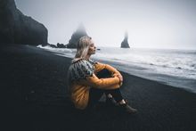 A woman with a yellow knit jumper sitting on black sand beach in Iceland