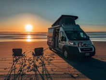 roadsurfer camper van with a raised roof parked on a beach.