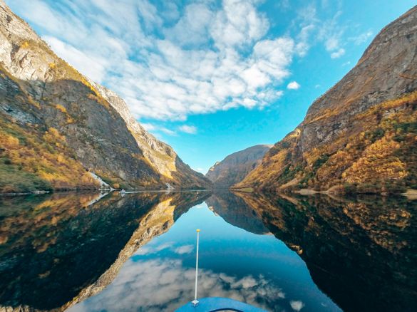 A view of Nærøyfjord in autumn colours, with the fjord and sky reflected in the water