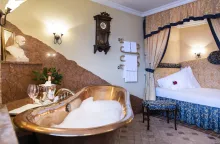 Romantik Hotel Im Weissen Rössl : A wooden bathtub filled with bubbles and a double bed in the background. 