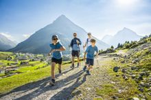 A family with two kids in athletic gear running on a mountain trail.