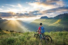 A woman sitting on a mountain bike in a grassy field with scenic mountains in St. Anton..