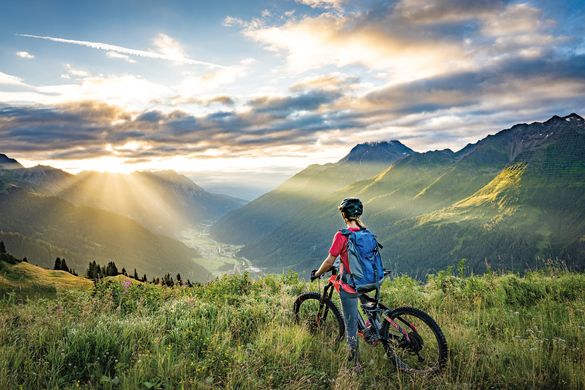 A woman sitting on a mountain bike in a grassy field with scenic mountains in St. Anton.. A woman sitting on a mountain bike in a grassy field with scenic mountains in St. Anton..