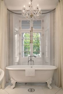Silvermine Suite encompasses an all-white bathroom with a stand-alone claw foot bathtub beneath a crystal chandelier