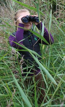 Girl with binoculars deep in a reed bed at a WWT Wetland Centre