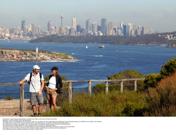 Couple walking along harbour at North Head, Manly, with views of Sydney city skyline