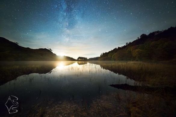 The setting moon casts a warm light over Loch Trool in the Galloway Forest Dark Sky Park, bringing out Autumn colours in the ancient Oak woodland. Overhead, the Milky Way sets into the West.
