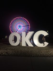 Media posed in front of the Wheeler Ferris Wheel at the OKC sign
